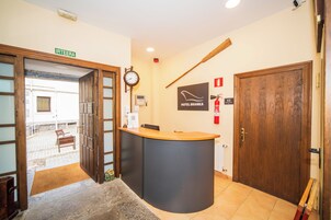 Zona de recepción con un mostrador de madera, un reloj y un cartel anunciando el Hotel Branka.