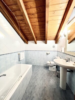 A bathroom with a bathtub, toilet, and sink, featuring wooden beams on the ceiling and tiled walls. - Hotel Branka (Mundaka)
