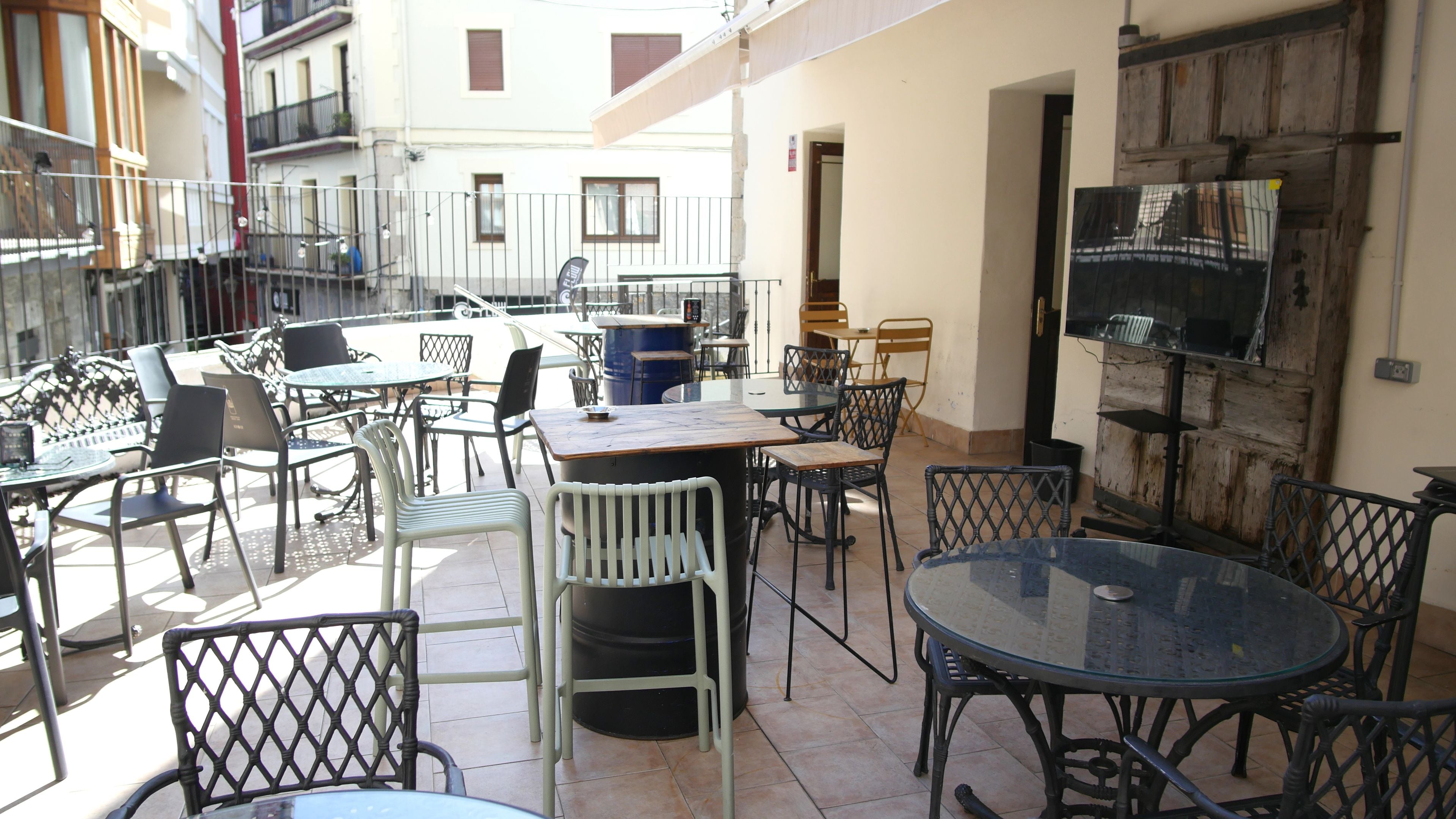 An outdoor patio area with tables and chairs, a large barrel, and a rustic wooden door.