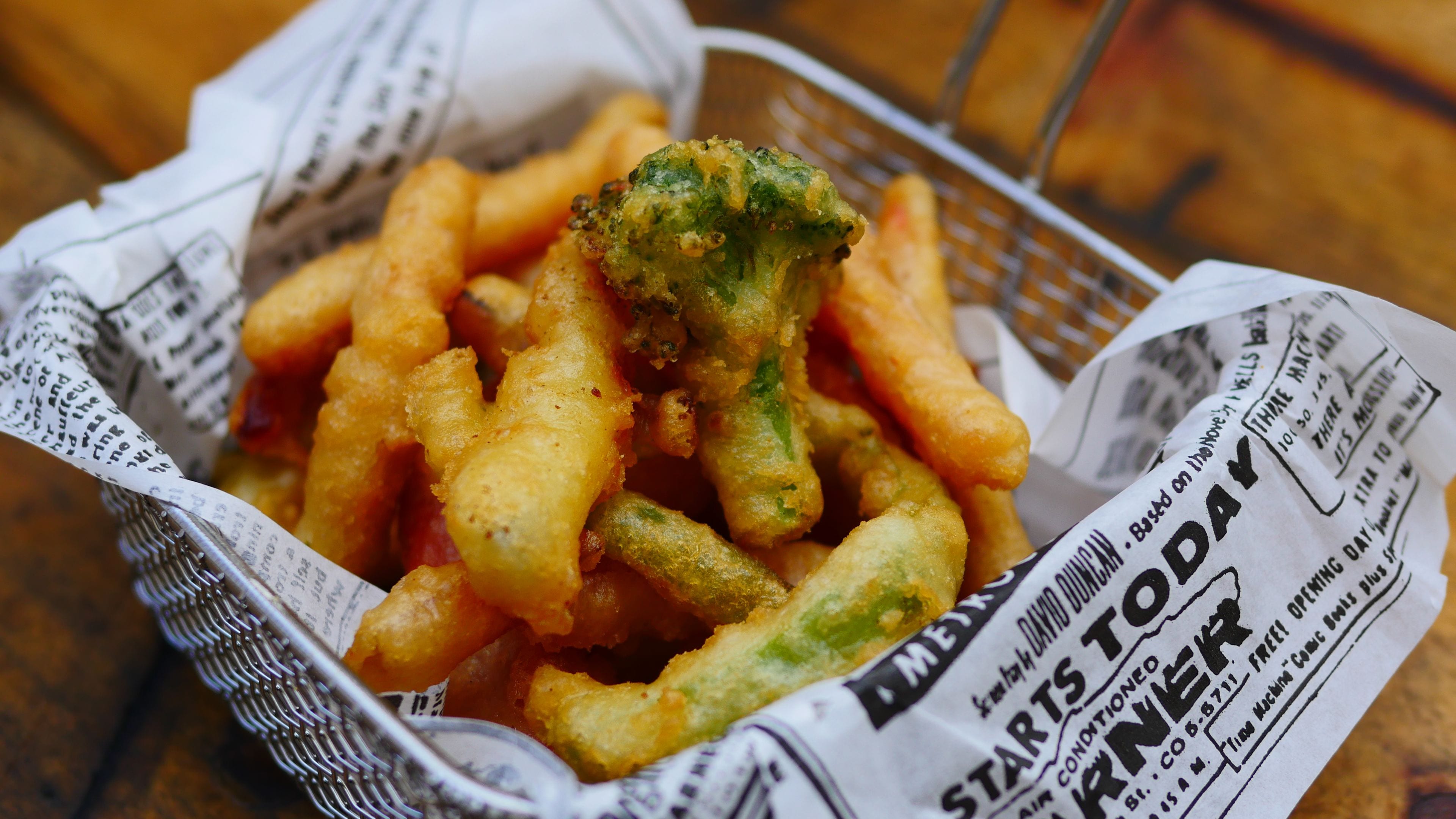 A basket of fried food items, possibly tempura, placed on a newspaper.