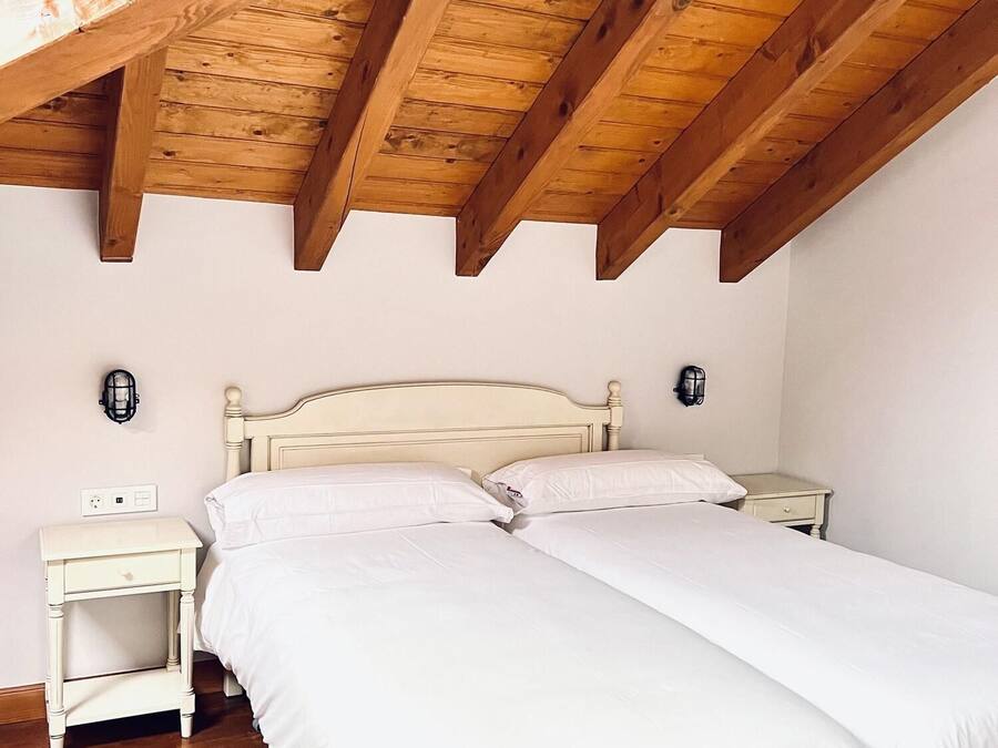 A bedroom with a wooden ceiling, a white bed, two bedside tables, and a nightstand.