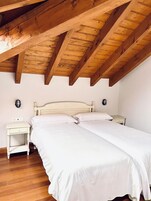 Un dormitorio con techo de madera, una cama blanca, dos mesitas de noche y una mesita auxiliar.
