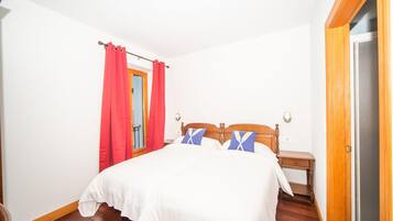 Un dormitorio con una cama de madera, ropa de cama blanca, una mesita de noche, un espejo y una cortina roja.