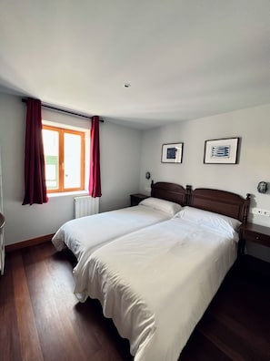 Una camera da letto con due letti, una finestra con tende rosse e due quadri appesi al muro.