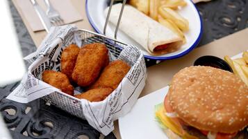 Una cesta de comida frita, un plato de papas fritas, un wrap y una hamburguesa sobre una mesa.