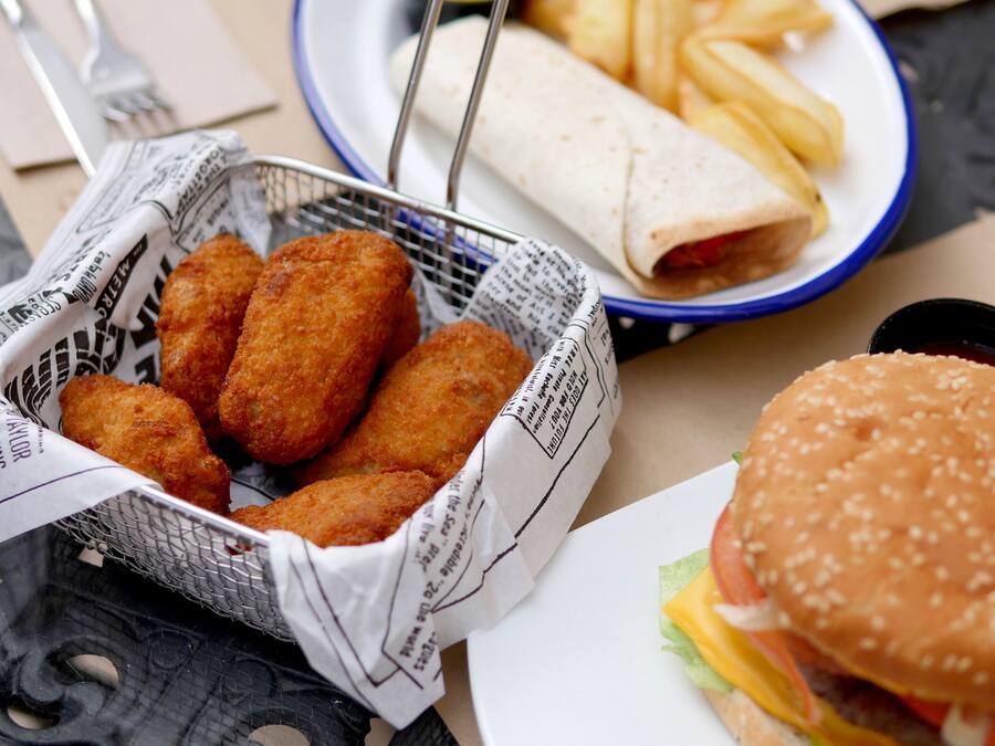 Una cesta de comida frita, un plato de papas fritas, un wrap y una hamburguesa sobre una mesa.