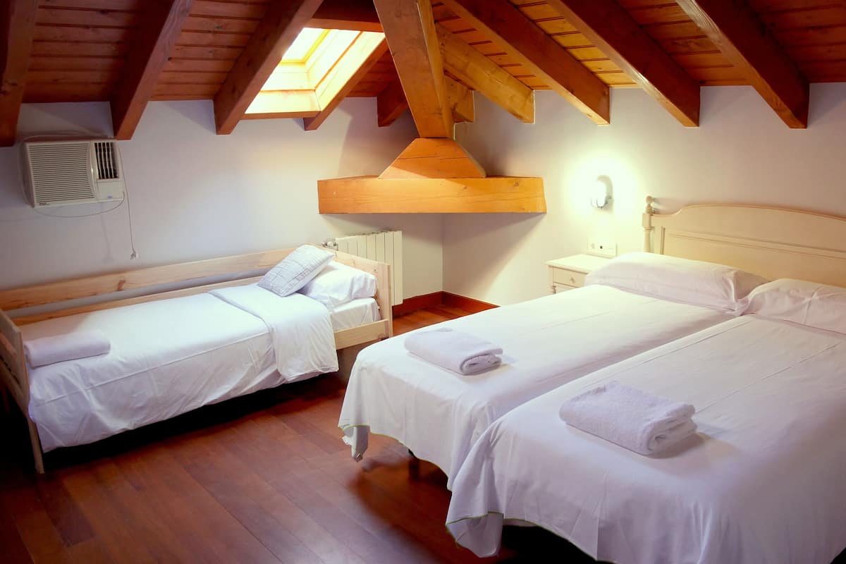 A room with two single beds, wooden beams, a skylight, and a radiator.
