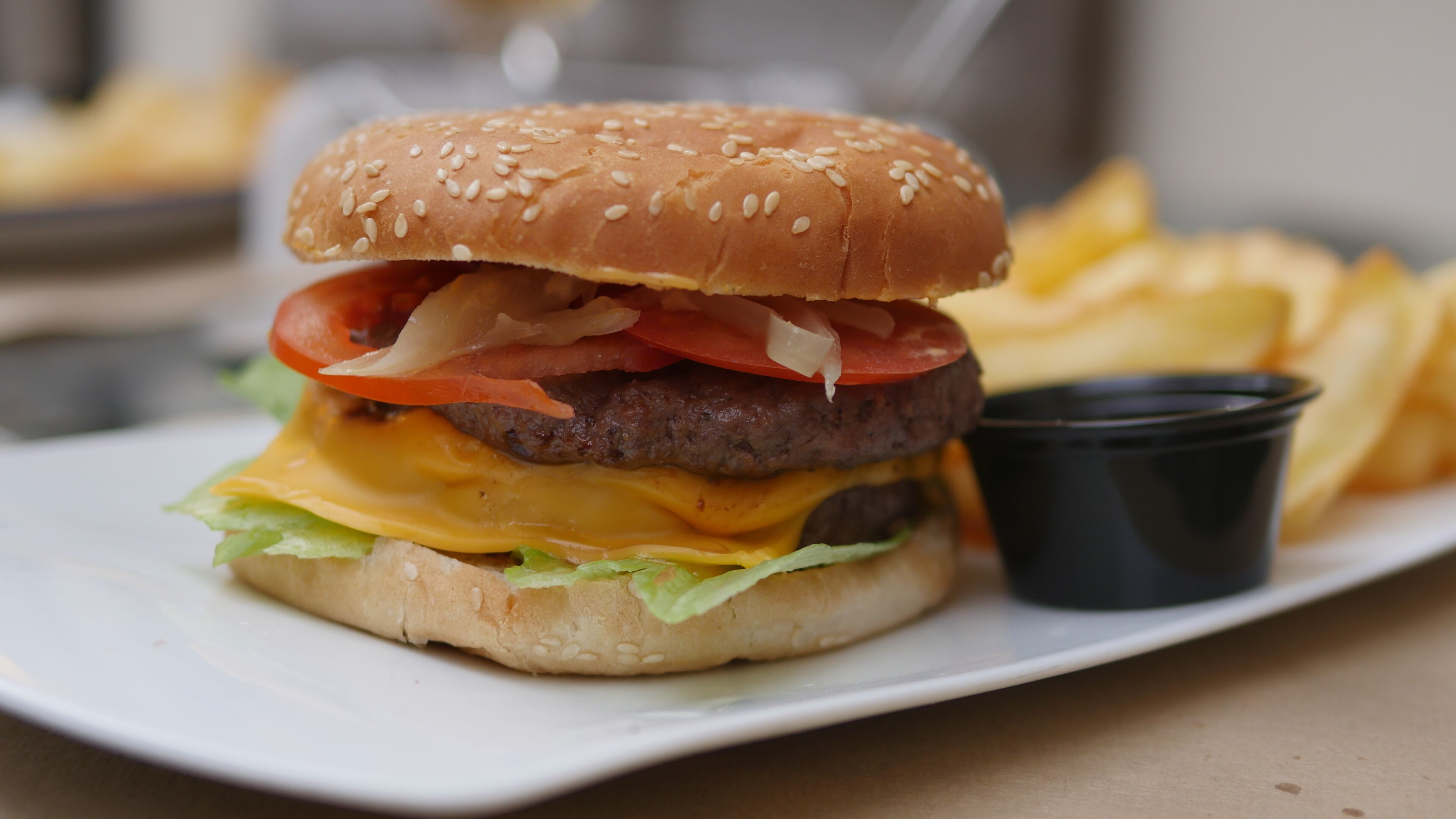 Hamburguesa con lechuga, tomate y queso, acompañada de papas fritas y una pequeña porción de salsa sobre un plato blanco.
