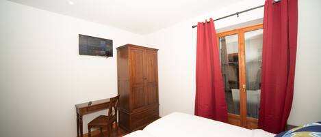 Une chambre à coucher avec un lit, une armoire en bois, un bureau et une fenêtre avec des rideaux rouges.