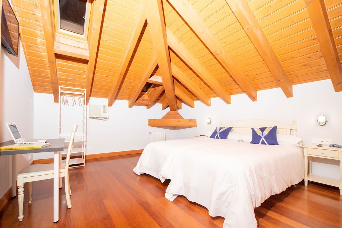 A bedroom with a wooden ceiling, a bed, a desk with a laptop, and a chair.