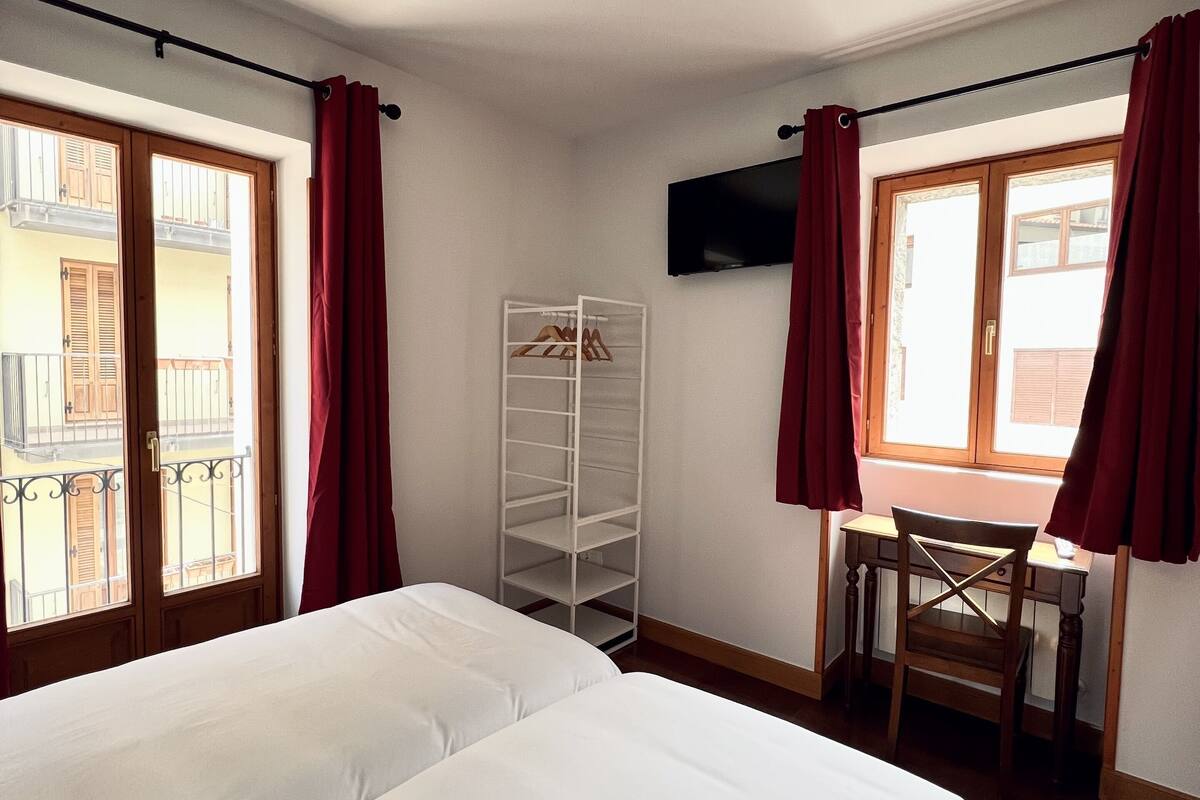 A hotel room with two beds, a desk, a chair, a TV, and a wardrobe.