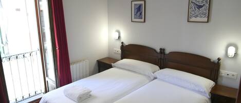 Habitación de hotel con dos camas individuales, una ventana con cortinas rojas y dos lámparas fijadas a la pared.