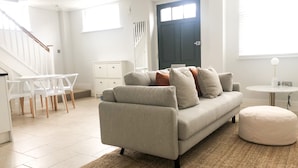 Ein modernes Wohnzimmer mit einem grauen Sofa, einem runden Hocker, einem weißen Couchtisch und einer Treppe, die zu einer weiteren Ebene führt.
