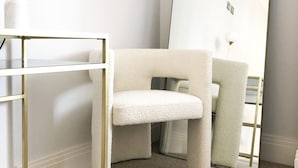 Ein minimalistisch eingerichteter Raum mit einem weißen Sofa, einem großen Spiegel und einem goldrahmigen Regal.
