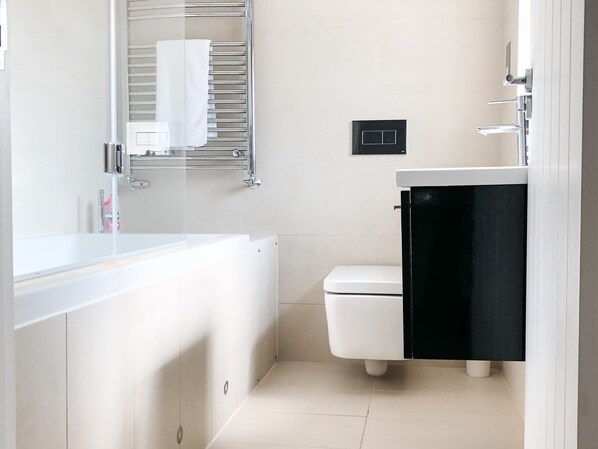 Un baño moderno con una bañera blanca, un inodoro blanco y un lavabo negro.