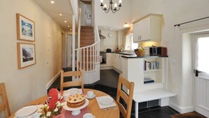 A dining area with a wooden table set for four, a chandelier, and a staircase leading to a kitchen. - The Barn, Park Farm near Chew Magna, Bristol (Bristol)