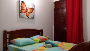 Ein Bett mit floralem Überwurf, zwei Kissen und ein gefaltetes Handtuch. An der Wand hängt ein Schmetterlingsbild.