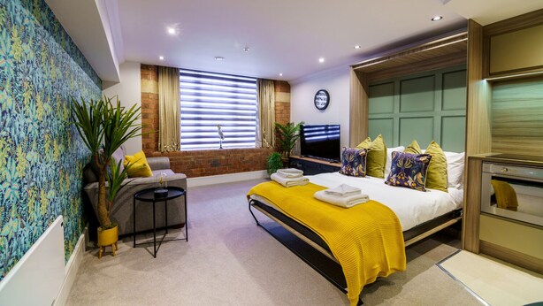 Une chambre d’hôtel moderne avec un grand lit, un petit bureau, une télévision et une fenêtre équipée de stores.