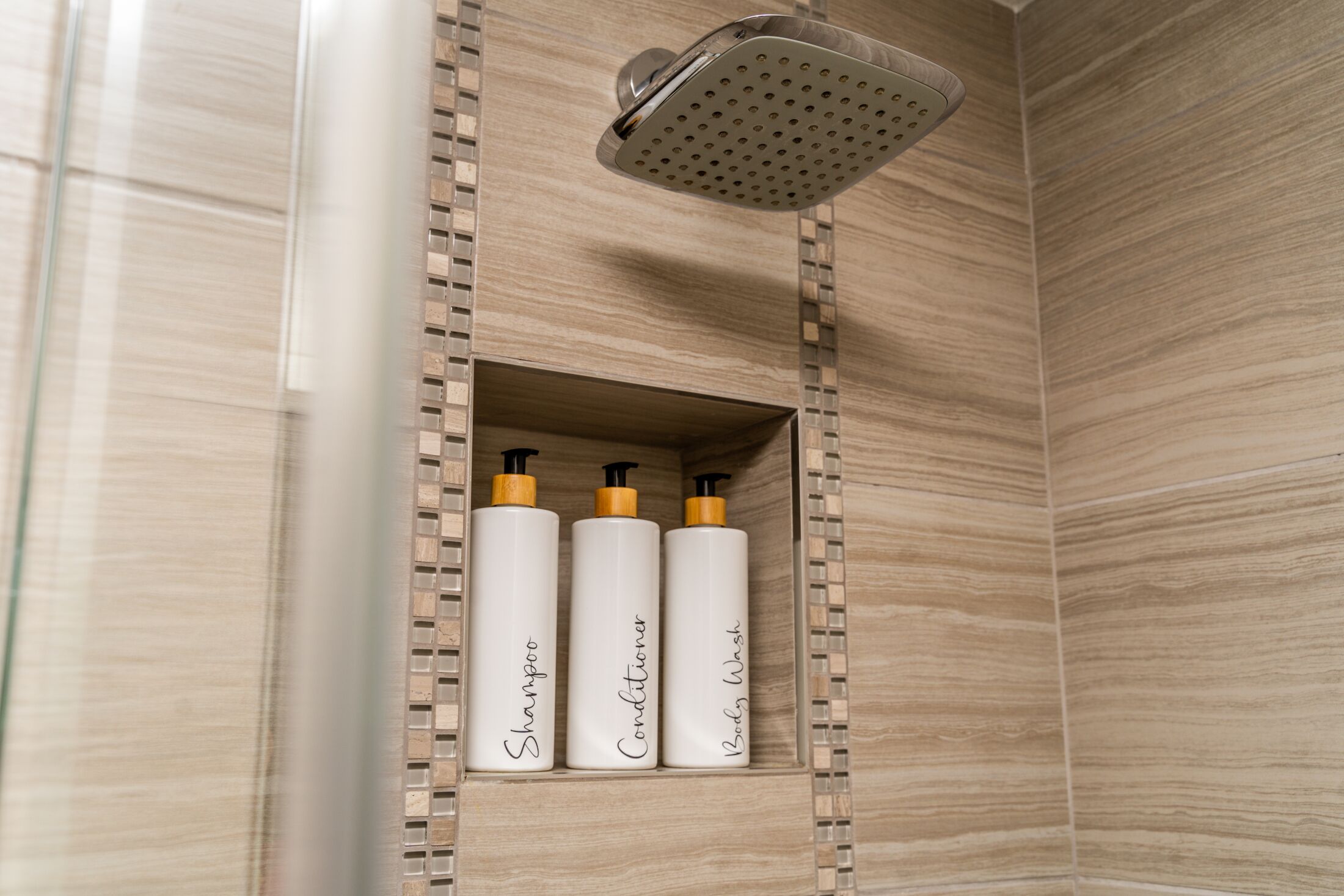 A bathroom with a showerhead, three bottles of shampoo, conditioner, and body wash.