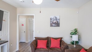 Ein Wohnzimmer mit braunem Sofa, roten Kissen, einer weißen Lampe und einem Gemälde an der Wand.