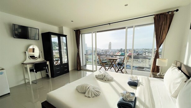 Une chambre d’hôtel avec un grand lit, un bureau avec un miroir, une armoire, une télévision et un balcon offrant une vue sur la ville.