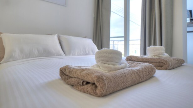 Une chambre d’hôtel avec un lit bien fait, deux serviettes, une fenêtre avec des rideaux et un tableau encadré au mur.