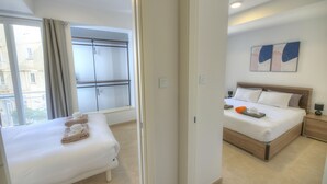 Une chambre d’hôtel comprenant un lit, une banquette, une fenêtre avec des rideaux, une table de chevet et une œuvre d’art accrochée au mur.