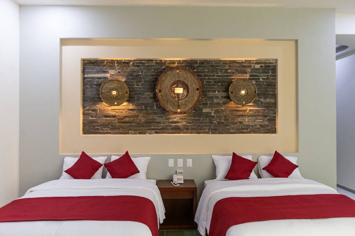 A hotel room with two beds, each with red and white bedding, and a large wall-mounted artwork above the beds.
