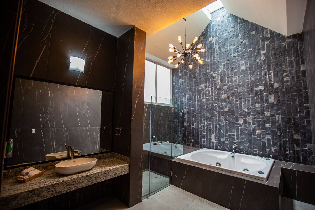 A modern bathroom with a large mirror, a freestanding bathtub, and a granite countertop.