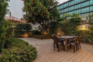 Un patio exterior con una mesa y sillas, rodeado de follaje y un edificio al fondo.