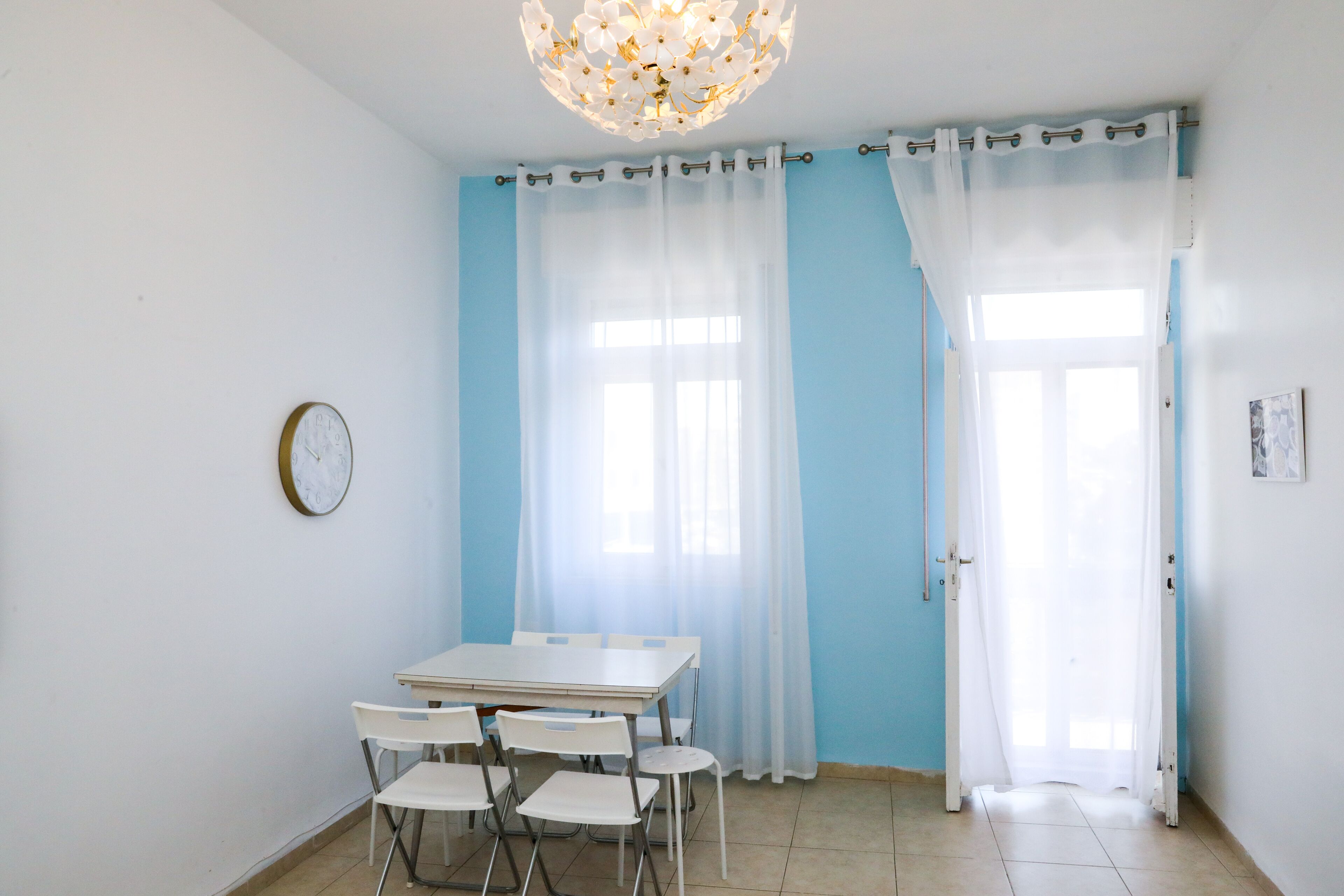 A room with a dining table and chairs, a clock on the wall, and a door with curtains.