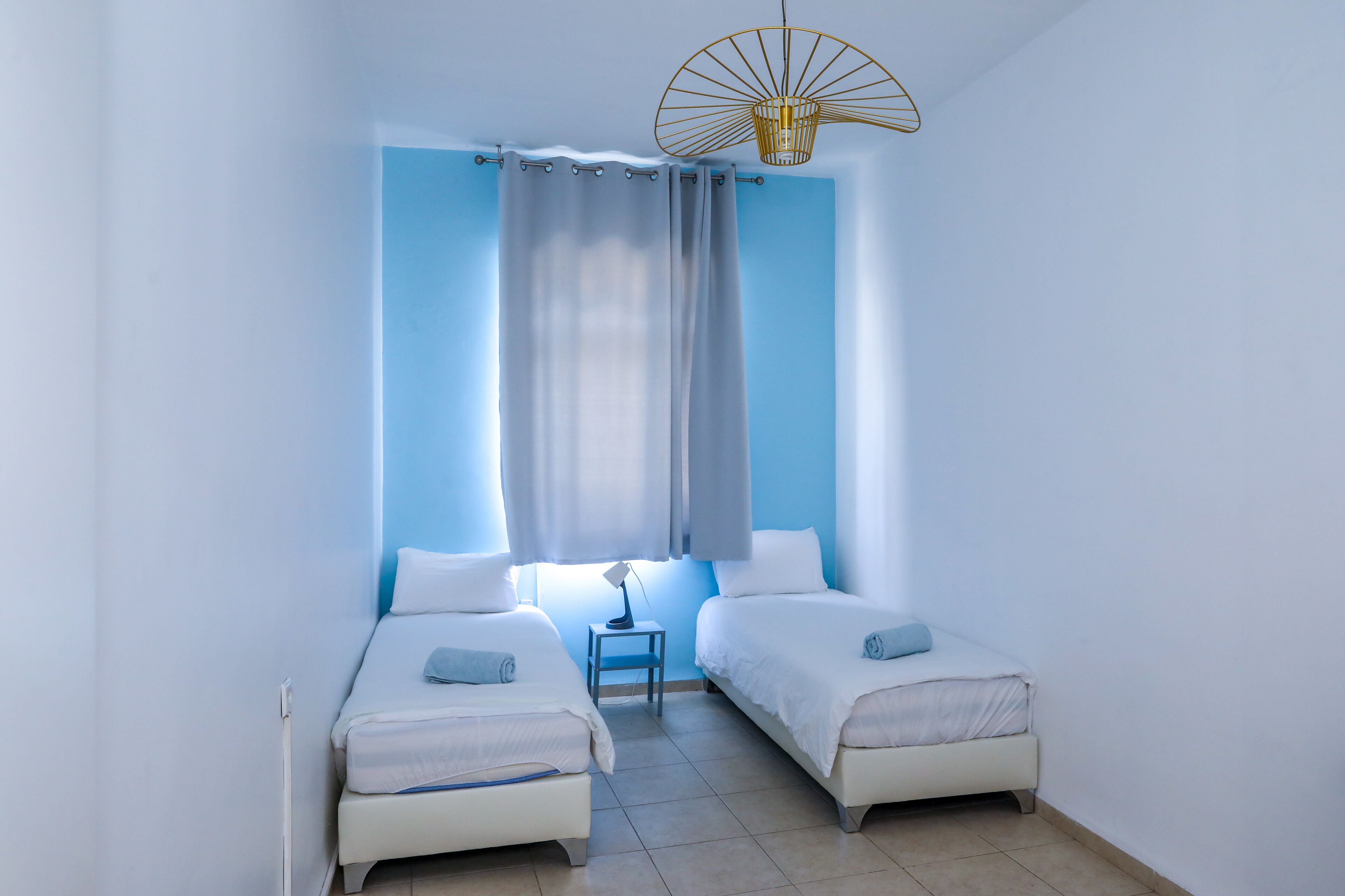 A room with two single beds, a small table, and a ceiling fan.