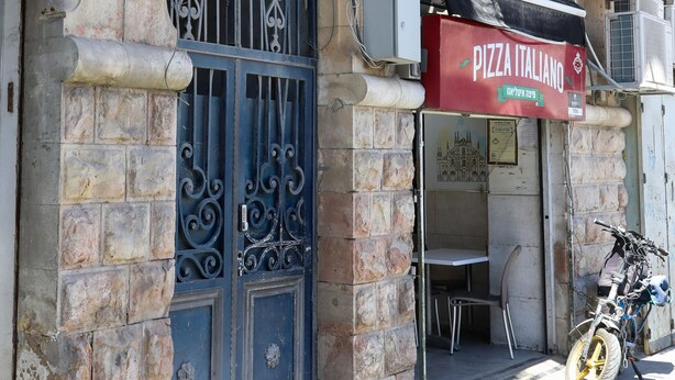 En bygning med en stenfassade, en metalport og et skilt til en pizzarestaurant.
