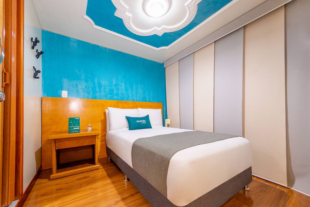 Une chambre d’hôtel avec un lit, une table de chevet en bois et un mur d’accent bleu.