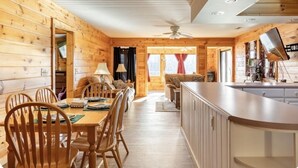 A wooden cabin interior with a dining area, kitchen, and seating space. - Sheep’s Knob Refuge- ..Take refuge in Him. Ps 34:8 (Franklin)