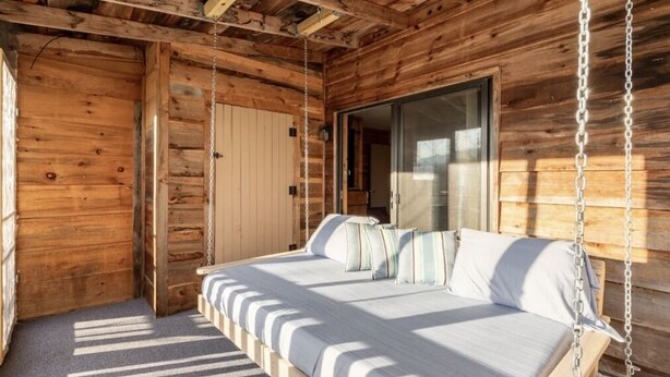 A wooden cabin room with a bed, a hanging chair, and a sliding door. - Sheep’s Knob Refuge- ..Take refuge in Him. Ps 34:8 (Franklin)
