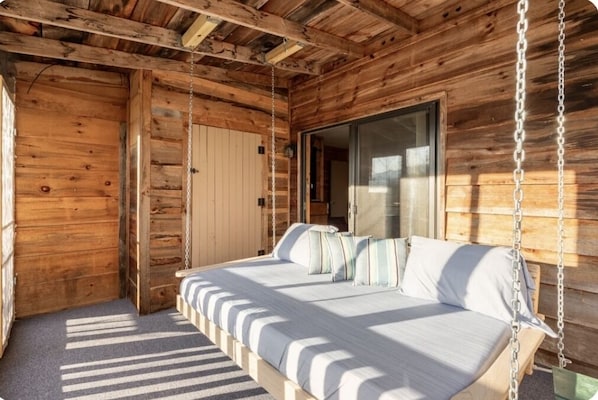 Relax in a cozy cabin with a unique suspended bed, surrounded by rustic charm and a large sliding door leading to an outdoor area.