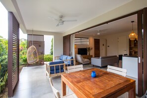 Un espace de vie moderne comprenant une table à manger en bois, un coin salon avec des canapés et des fauteuils, un téléviseur et un ventilateur de plafond.