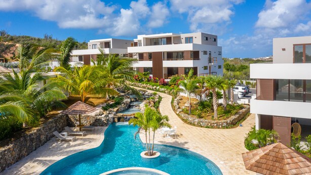Een resort met een zwembad, palmbomen en moderne gebouwen.
