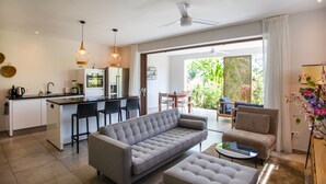 Een moderne woonkamer met een bank, voetenbankje en salontafel, een keuken met barkrukken, en een eetgedeelte met een tafel en stoelen.