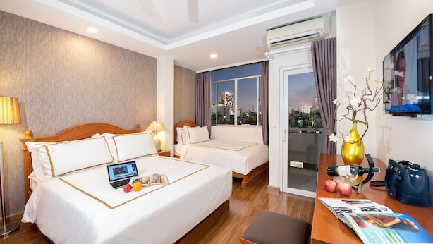 A hotel room with two beds, a desk with a laptop, a vase with flowers, and a city view. - Me Gustas Downtown Hotel (Ho Chi Minh City)