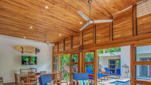 Un intérieur en bois comprenant un coin repas, des ventilateurs de plafond et une vue sur l’extérieur.
