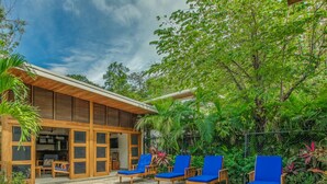 Une maison moderne dotée d’une piscine, de fauteuils de jardin bleus et d’une végétation luxuriante.