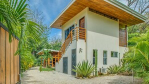 Une maison moderne à deux étages, avec une façade en bois, un escalier menant à l’étage supérieur et un jardin bien entretenu où poussent différentes espèces de plantes.
