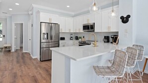 A modern kitchen with white cabinetry, stainless steel appliances, and a central island with bar stools.