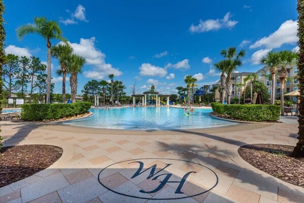 A swimming pool with a pavilion, surrounded by palm trees and a clear blue sky.