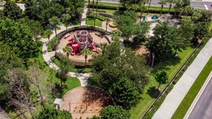 An aerial view of a park with a playground, surrounded by trees and a road.