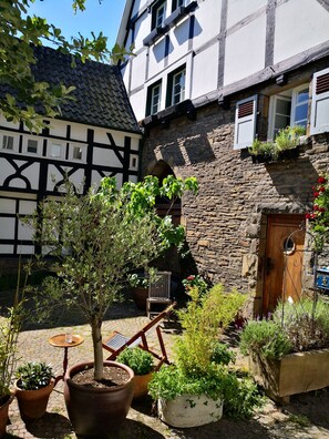 A courtyard with a tree, potted plants, a wooden chair, and a stone wall.