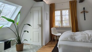 A bedroom with a bed, a desk, a chair, a potted plant, and a window with curtains. - Fünf Giebel Eck in der Freiheit am Ruhrtalradweg (Wetter)