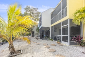 A modern building with a covered outdoor area, palm trees, and a gravel path.